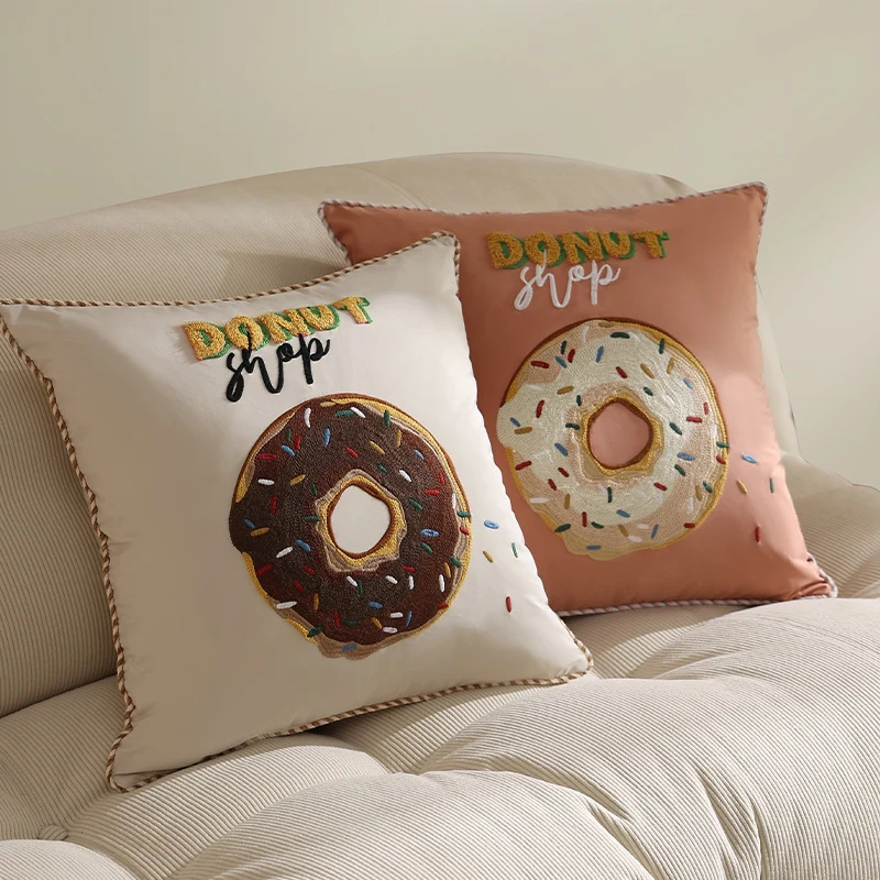 Quadratisches Dekokissen mit gesticktem Donut-Motiv und dekorativer Kederkante